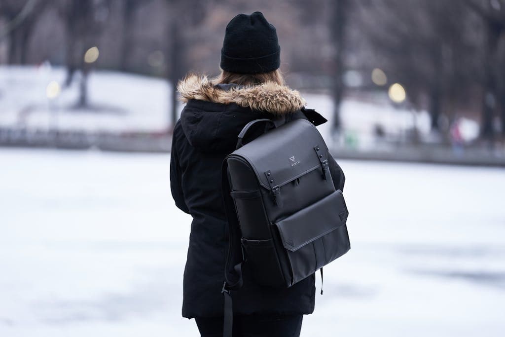 A woman in a black winter jacket explores a snowy park with a stylish backpack.