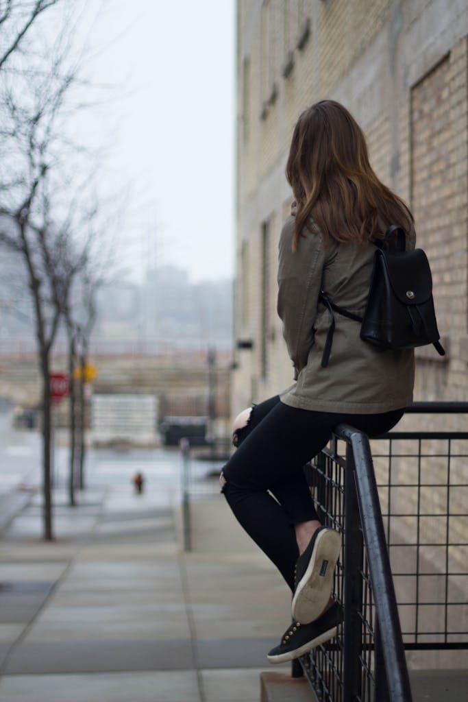 Casual young woman sitting on railing overlooking urban street scene. Modern and fashionable attire.
